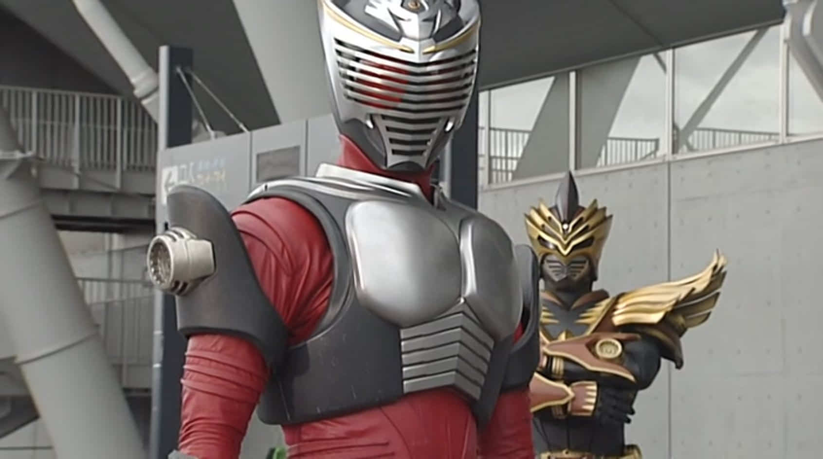 Kamen Rider Odin stands behind Kamen Rider Ryuki, the latter about to deliver a surprise blow to the former.